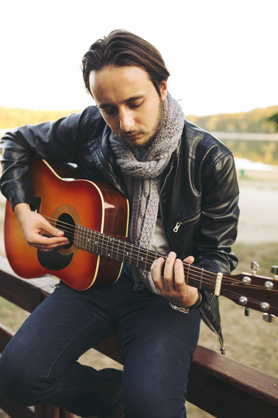 Young man playing on guitar at the lake - Photo, Image