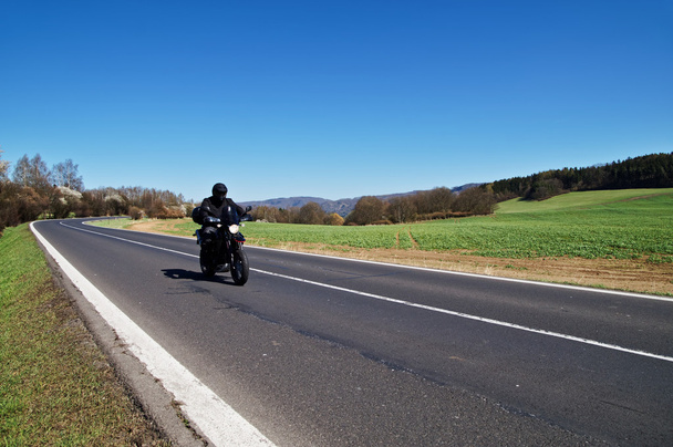 Black motorcycle traveling on the asphalt road in rural landscape in early spring - Photo, Image