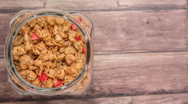 Breakfast cereal with dried raspberry pieces in glass jar over wooden background - Photo, Image