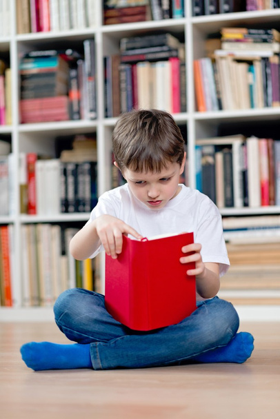 Little boy child reading a red book in the library. - Foto, Imagen