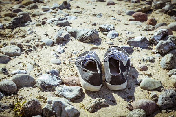 twee oude schoenen bij een stenige strand - Foto, afbeelding