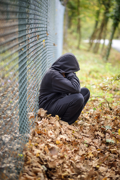tel çit kapüşonlu genç önünde oturan - Fotoğraf, Görsel
