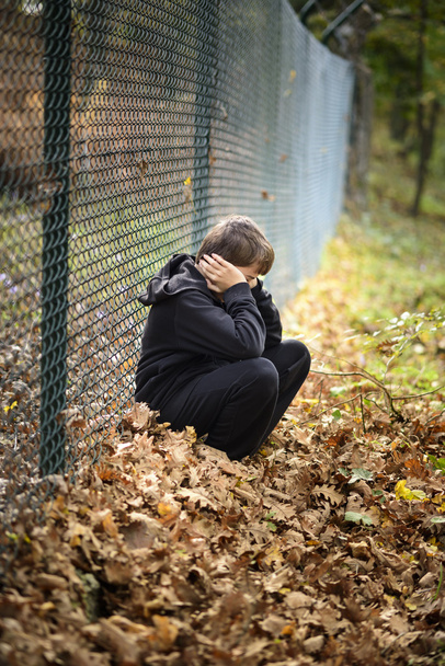 verdrietig kind zitten voor een draad hek - Foto, afbeelding