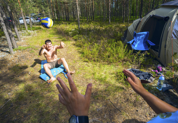 jonge man gooit een bal zittend op tapijt bossen in het gazon. - Foto, afbeelding