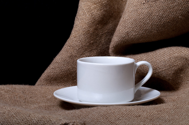 Cup and saucer on a burlap a black background - Foto, afbeelding