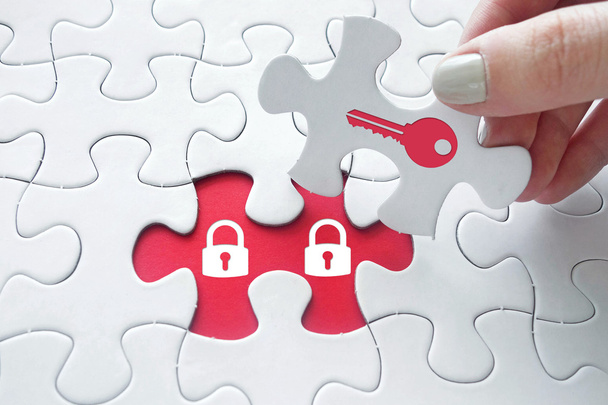 Close up of girl's hand placing the last jigsaw puzzle piece with key and padlock symbol as security concept - Zdjęcie, obraz