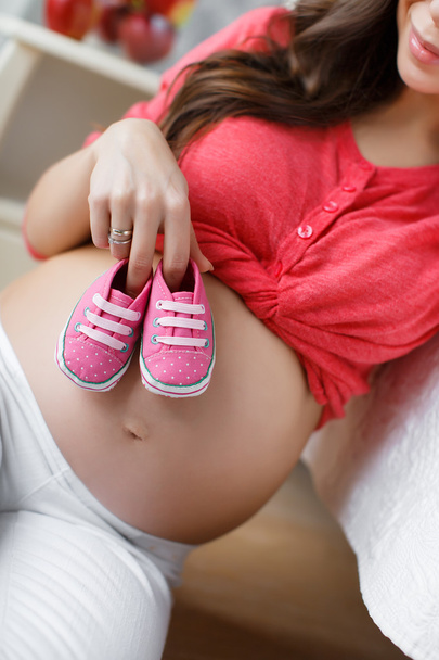 Gelukkig toekomstige moeder met roze schoentjes in de hand - Foto, afbeelding