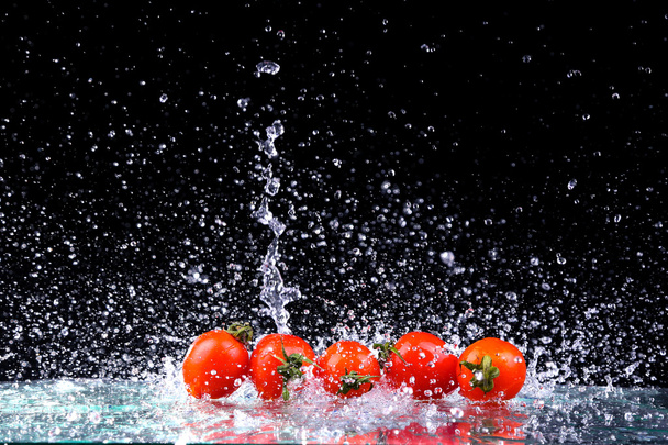 Łapka z zamrożenia ruchu Pomidory czereśniowe w plusk wody na czarnym tle z kopii przestrzeni - Zdjęcie, obraz