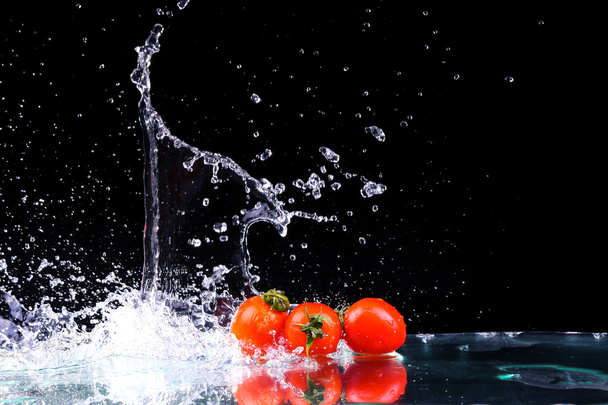 Studio shot with freeze motion of cherry tomatoes in water splash on black background with copy space - Фото, изображение
