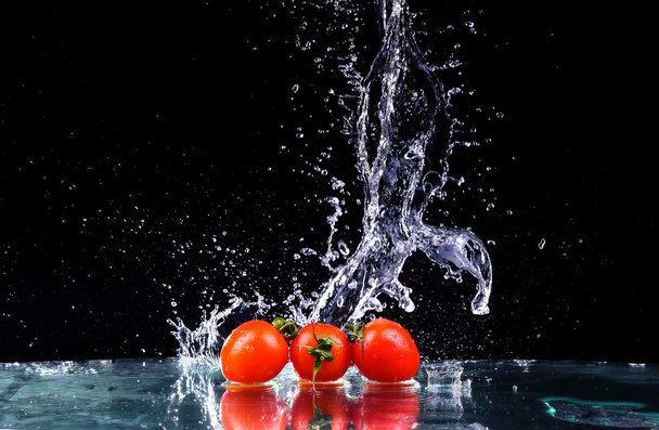 Студийный снимок с замораживающим движением помидоров черри в водяном брызге на черном фоне с копировальным пространством
 - Фото, изображение