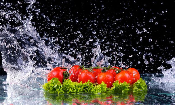 Свіжий помідор вишня і зелений свіжий салат з водяним крапельним бризом на темному тлі Макро краплі води падають на червоні вишневі помідори і роблять бризки
 - Фото, зображення