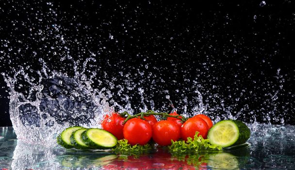 Studio shot with freeze motion of cherry tomatoes and slices of cucumber in water splash on black background - Photo, Image