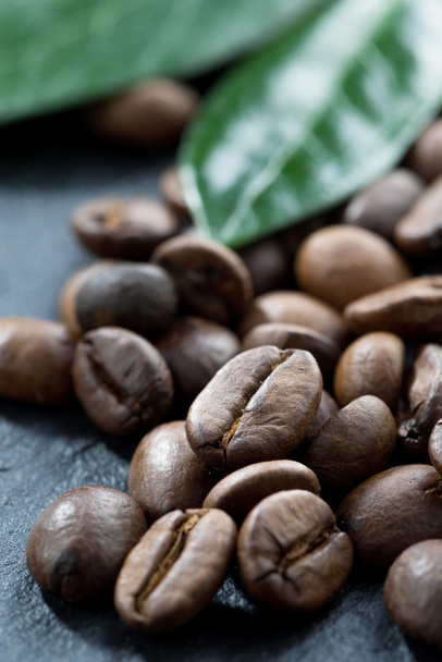 pražená kávová zrna a listy na tmavém pozadí, detail - Fotografie, Obrázek