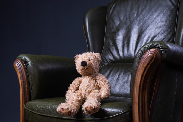 Teddy bear sits in a green leather armchair in front of the wall - Foto, immagini