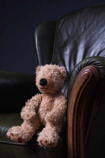 Teddy bear sits in a green leather armchair in front of the wall - Valokuva, kuva