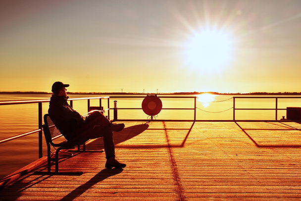 Homme assis sur le quai et profiter de la matinée en mer. Ciel bleu clair ensoleillé, niveau d'eau lisse
 - Photo, image