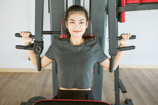 Азиатская женщина упражнения на плече пресс-машины в тренажерном зале
 - Фото, изображение