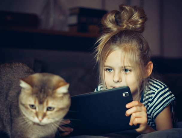 Hermosa chica sosteniendo una tableta y mira al gato
 - Foto, imagen