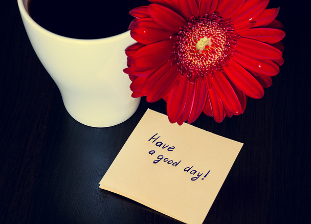 Red gerbera flower, cup of coffee and paper with text "Have a g
 - Фото, изображение