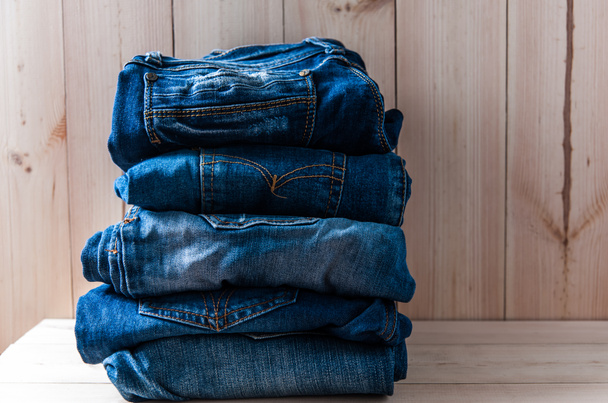 Nahaufnahme vieler Jeans-Hosenstapel auf Holzgrund - Foto, Bild