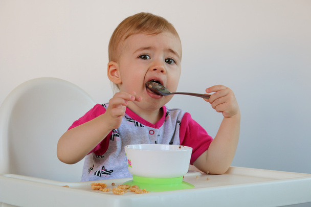 kleines lächelndes Baby sitzt im Hochstuhl und isst Haferbrei auf Teller. - Foto, Bild