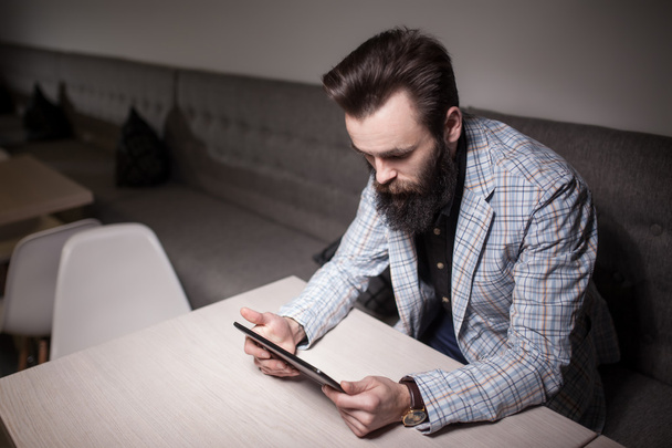 bearded man in suit and with tablet sitting in cafe and browsing - Foto, Imagem