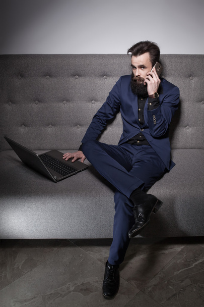 bearded man dressed in suit and with laptop and talk on phone; - Fotó, kép