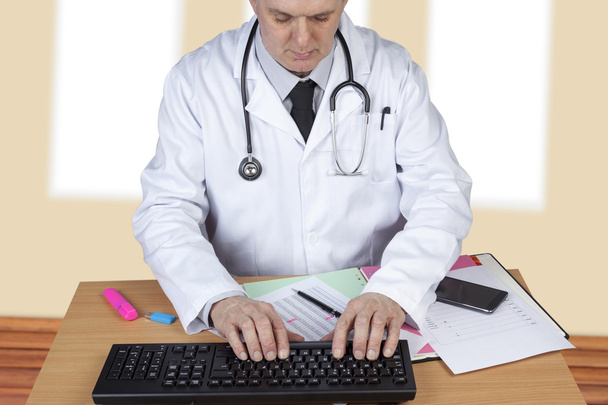 Doctor with stethoscope around his neck typing up a report - Fotó, kép