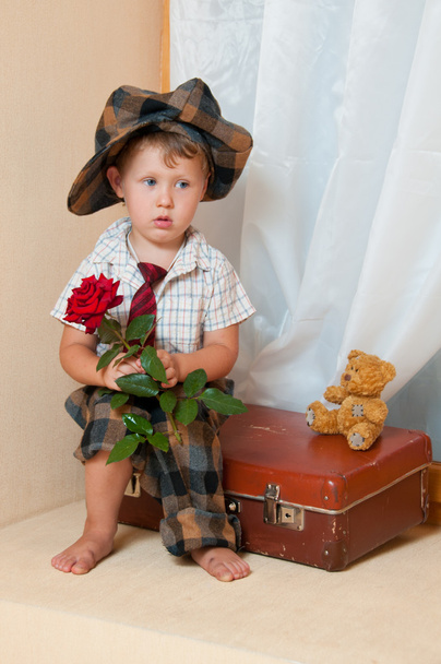 Cute little boy with the flower sitting on an old suitcase. He i - Photo, image