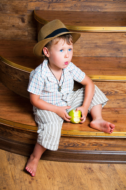 A cute boy with an apple in his hand sitting on the steps. - Foto, Imagen