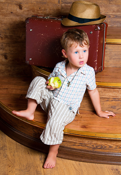A cute boy with an apple in his hand sitting on the steps. - 写真・画像