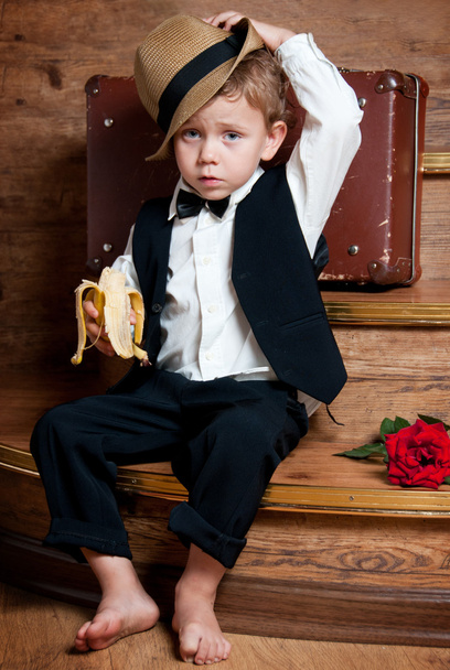 Cute little boy with a banana in his hand sitting on the steps. - Φωτογραφία, εικόνα