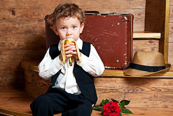 Cute little boy with a banana in his hand sitting on the steps. - Fotografie, Obrázek
