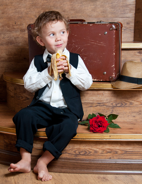 Cute little boy with a banana in his hand sitting on the steps. - 写真・画像