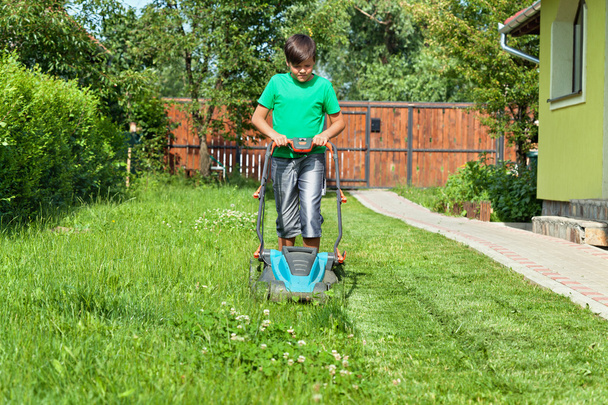 Poika leikkaa nurmikkoa ympäri taloa kesällä
 - Valokuva, kuva