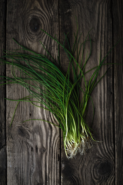 Stalks of green onions on a wooden table - Fotó, kép