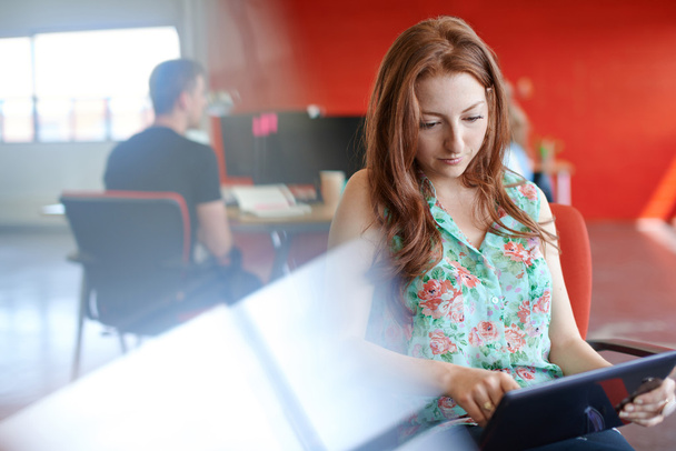 Vertrouwen vrouwelijke ontwerper werkt aan een digitaal tablet in rode creatieve kantoorruimte - Foto, afbeelding
