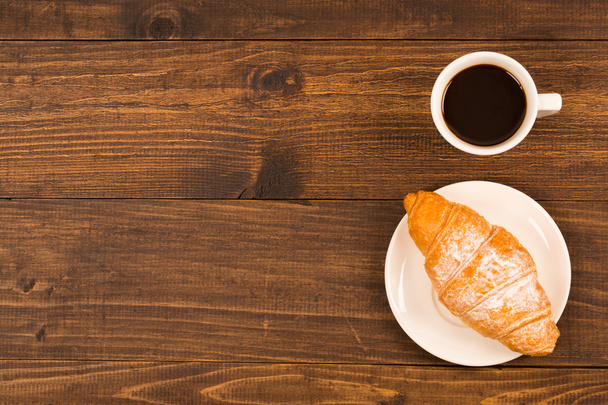 Tazza da caffè con croissant per colazione su un tavolo di legno scuro, vista dall'alto
 - Foto, immagini