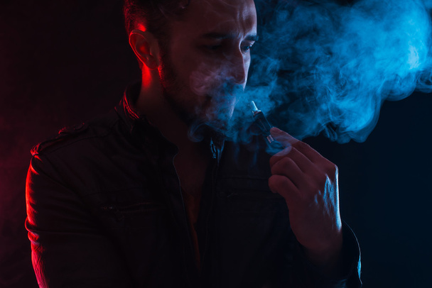 бородатый стильный мужчина держит и курит электронную сигарету
 - Фото, изображение