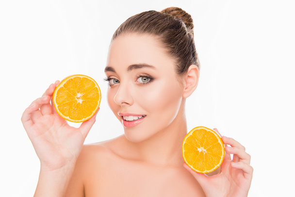 Smiling young pretty woman holding two halves of orange - Zdjęcie, obraz