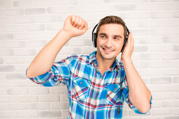 Mladý usměvavý muž poslouchající hudbu ve sluchátkách - Fotografie, Obrázek