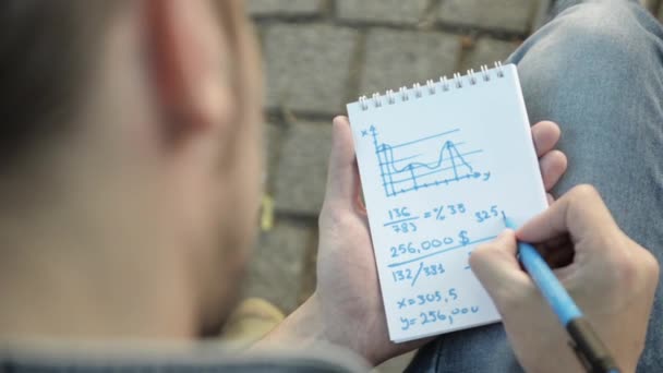 Main de l'homme dessine des tâches mathématiques par marqueur bleu sur le carnet papier, tourner la page. Vue du dessus
 - Séquence, vidéo