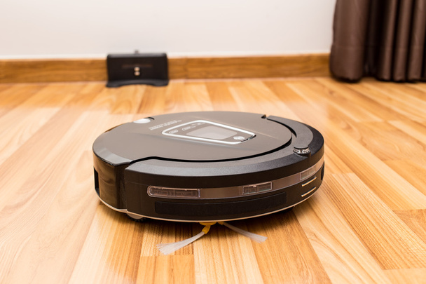 Robotic vacuum cleaner on wood parquet floor. - Foto, afbeelding