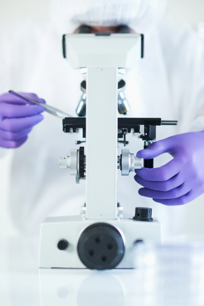 Científico llevando a cabo investigación en laboratorio estéril mientras mira a través del microscopio enfoque selectivo
 - Foto, Imagen