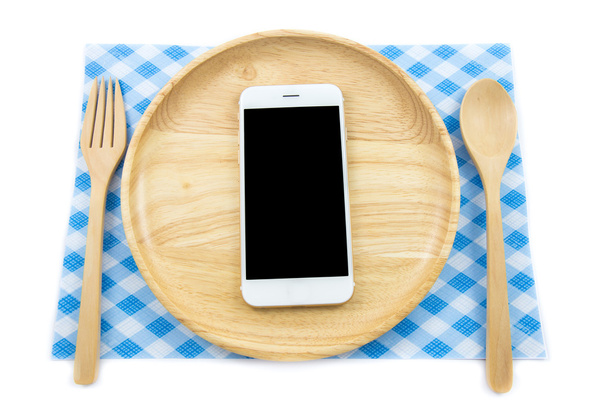 Bovenaanzicht smartphone op houten schotel met spon en vork op witte achtergrond, begrip etend technologie - Foto, afbeelding