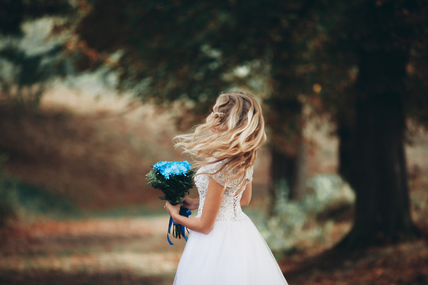 Beautiful young blond bride with bridal bouquet sitting on the stairs under gorgeous plants - Φωτογραφία, εικόνα