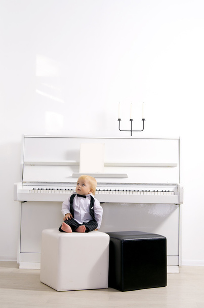 Хлопчик у костюмі сидить на білому піаніно
 - Фото, зображення