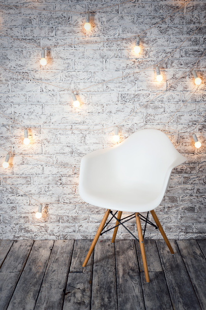 Empty white chair against the backdrop of a brick wall with a garland of light bulbs. - Fotoğraf, Görsel