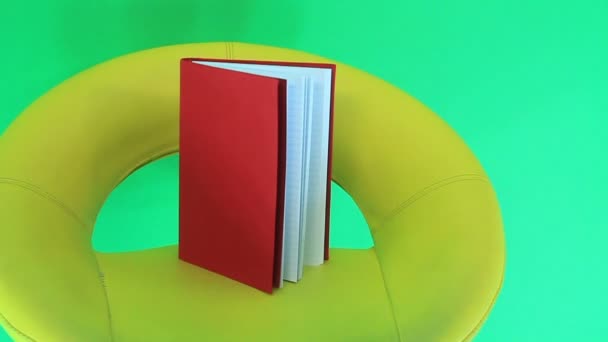 Bir iskemle Isolated yeşil zemin üzerine kırmızı kitap. - Video, Çekim