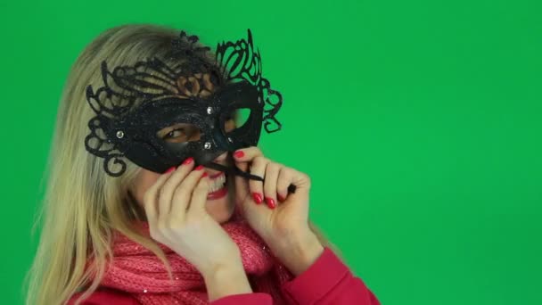 Woman having fun measures the carnival venetian mask on the green background - Video